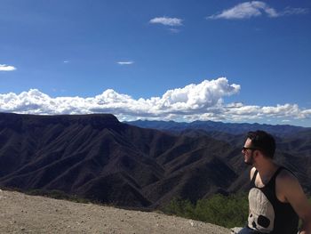 Man sitting by mountains against blue sky