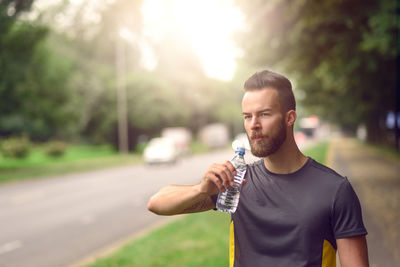 Handsome athlete drinking water by road