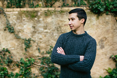 Smiling young man with arms crossed looking away while standing in park