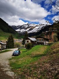 Cars on street amidst houses against buildings and mountains against sky