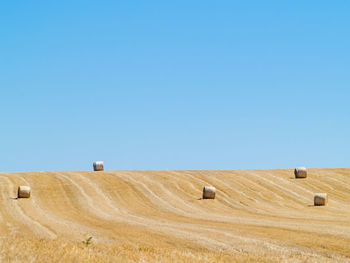 Hay bales on field against clear blue sky