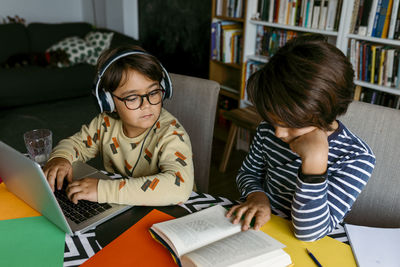 Rear view of siblings sitting on table at home