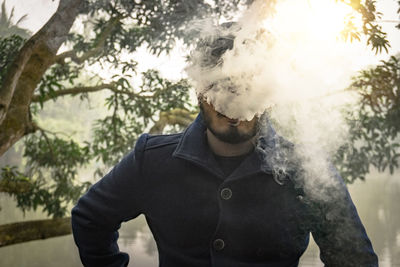 Man smoking while standing against tree and lake