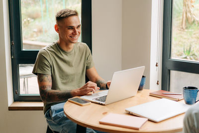 Portrait of a laughing young business man working remotely on a laptop while sitting at home.