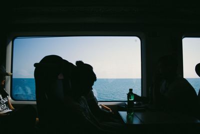 Silhouette people sitting in sea seen through window