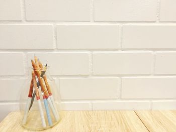 Pencils in container on table against wall