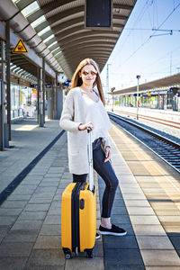 Full length of woman standing with luggage at railroad station platform