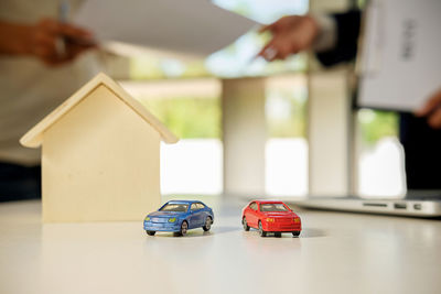 Close-up of toy cars and model home on table against client and salesman with documents