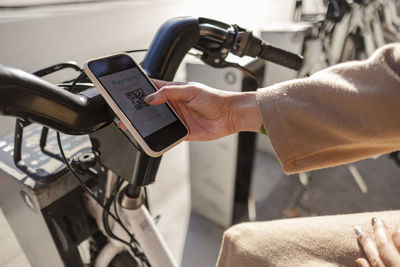 Young woman scanning qr code for renting bicycle