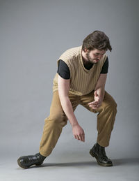 Full length of young man sitting against gray background