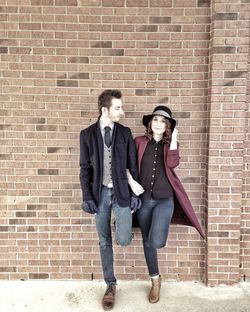 Fashionable young couple leaning on brick wall in city