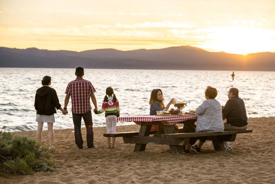 Rear view of people sitting on beach at sunset