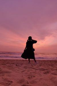 Rear view of woman standing at beach against sky during sunset