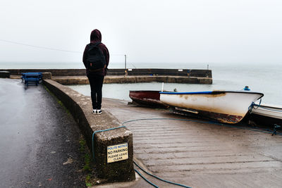 Rear view of teenage girl with backpack standing on retaining wall by sea against sky