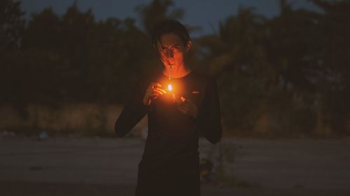 Side view of woman holding sparkler at sunset