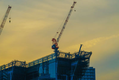 Low angle view of crane at construction site during sunset