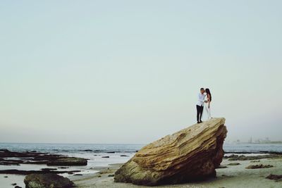 Young woman standing on rock by sea against sky