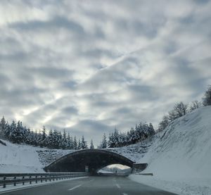 Snow covered road by trees against sky