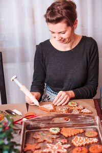 Woman smiling while decorating christmas gingerbread cookies at home