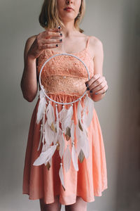 Midsection of young woman holding dreamcatcher against gray wall