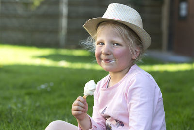 Portrait of cute girl eating ice cream while siting on field at park