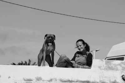 Portrait of happy woman with boxer on retaining wall against sky