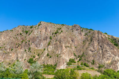 Low angle view of rocky mountain against clear blue sky