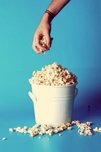 Cropped hand of man having popcorn in bucket against blue background