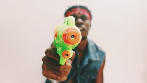 Young man playing with squirt gun against white background