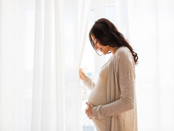 Side view of woman standing against curtain