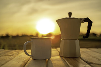 Coffee cup on table against sky during sunset