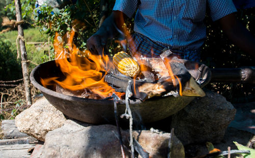 Midsection of man cooking corn on fire pit