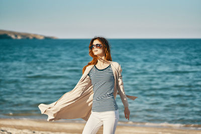 Woman wearing sunglasses standing at beach against sky