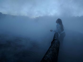 Reflection of person on mountain against sky during foggy weather