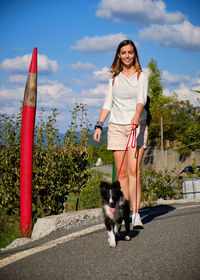 Portrait of young woman with dog standing against sky