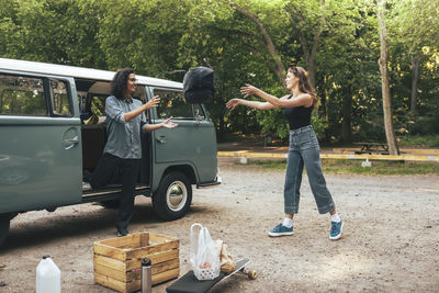 Male and female friends throwing backpack while standing outside camping van