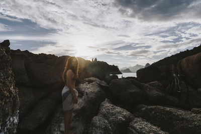 Portrait of young woman standing on rock formations against sky