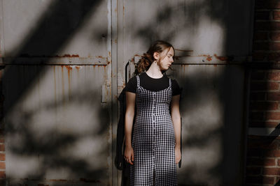 Teenage girl with eyes closed standing against rusty metallic wall