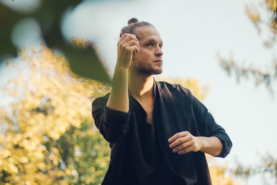 Thoughtful young man looking away while standing against plants