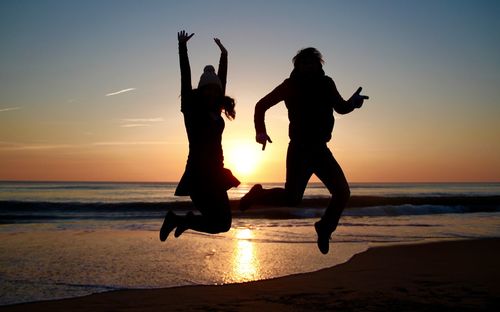 Silhouette people jumping on beach against sky during sunset