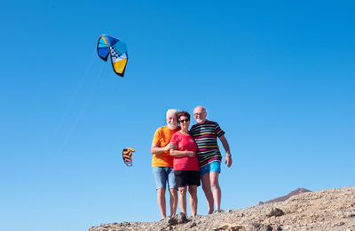 Low angle portrait of happy friends standing at beach against clear sky