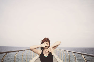 Young woman standing in front of sea against clear sky