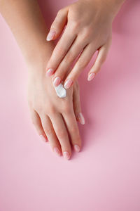 A young woman is applying cream to her hands. spa and body care concept on pink background.