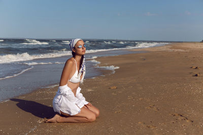 Woman in a white bathing suit and hat sunglasses on an empty sandy beach