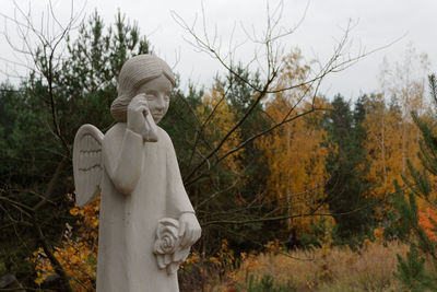 Statue of angel against trees and plants