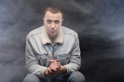 Portrait of young man sitting against gray background