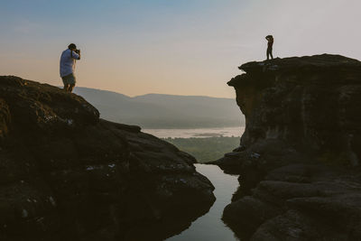 Women standing on rock by mountain against sky