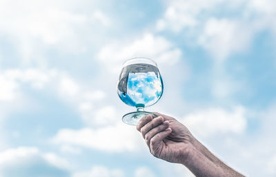 Low angle view of hand holding glass against sky