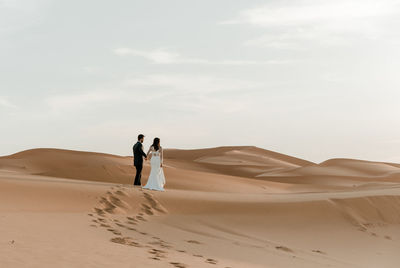 People on sand dune in desert against sky