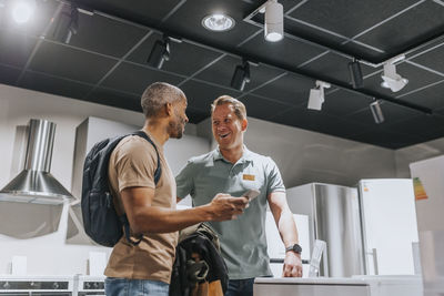 Salesman and customer laughing while discussing over smart phone in electronics store